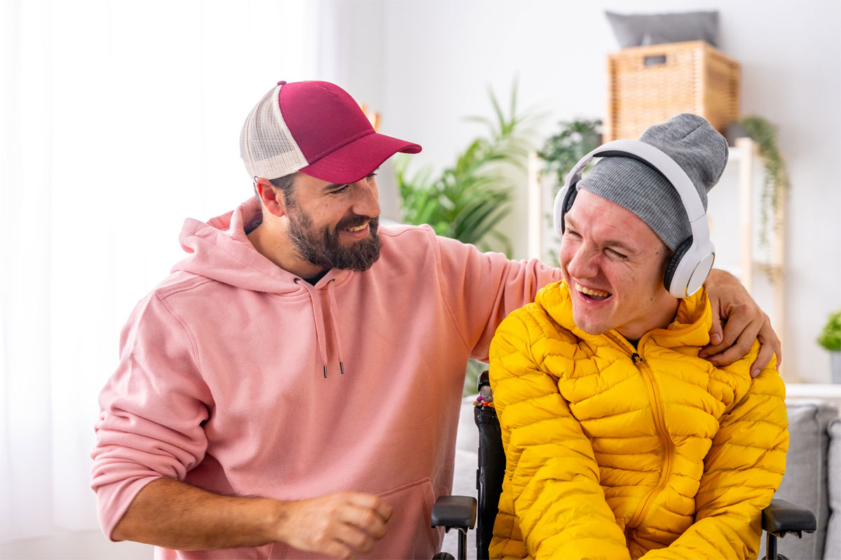 Man in salmon hoodie supported another in yellow jacket with headphones