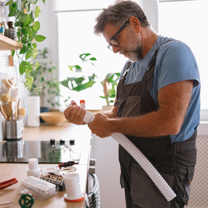 Plumber repairing pipes in bright kitchen